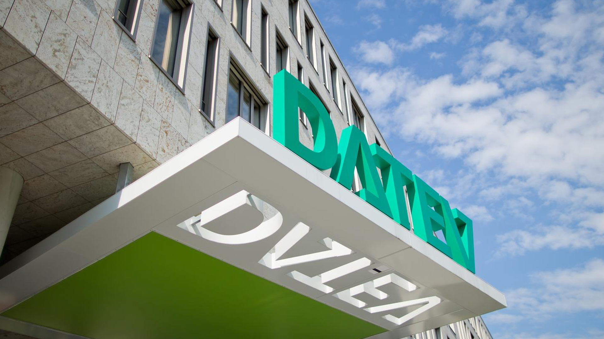 Eingang eines Bürogebäudes mit grünem DATEV-Schriftzug auf weißem Vordach, Blick nach oben.